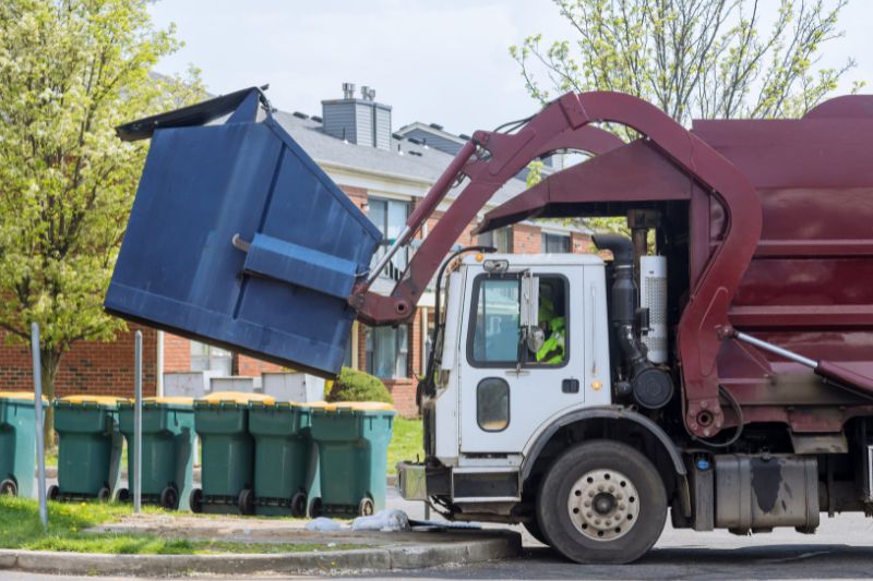 Side-loader garbage truck servicing a city street at dawn